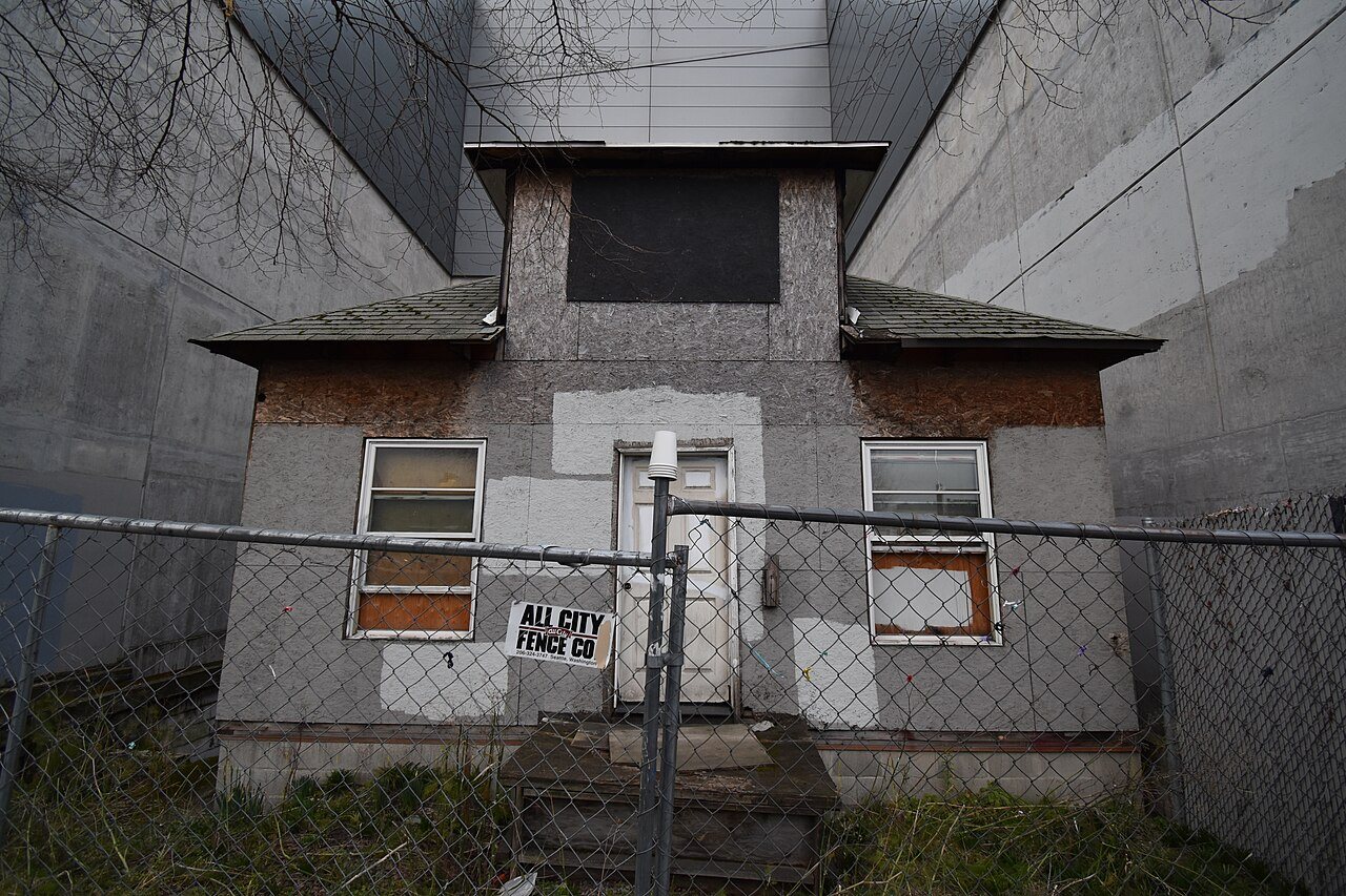 The small gray Edith Macefield house in Seattle's Ballard neighborhood, its windows partly boarded, behind a chain-link fence and boxed in by the tall concrete walls of a commercial building